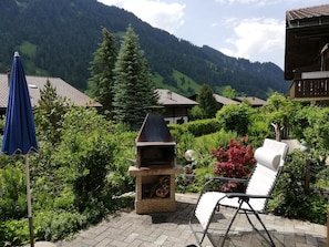 A patio with a barbecue grill, a folding chair, and a blue umbrella. - Chalet Flöschhorn Appartement/Fewo, Bad, WC, 3 Schlafräume by Interhome (Lenk)