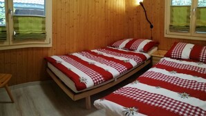 Ein Zimmer mit Holzboden und zwei Betten, jeweils mit einer rot-weiß karierten Tagesdecke und passenden Kissen.