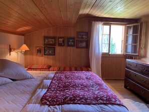 Een slaapkamer in een houten blokhut met een bed, een dressoir en een raam met gordijnen.