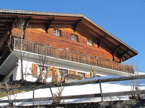 Een houten chalet met een balkon, omgeven door sneeuw.