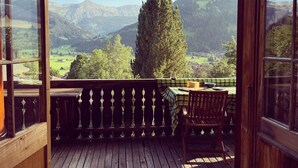 A wooden deck with a table and chairs, overlooking a mountainous landscape with a large tree and a village below. - Steirösli 1. & 2. Stock Appartement/Fewo, Dusche und Badewanne, 4 oder mehr Schl by Interhome (Lenk)