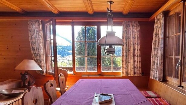 A wooden cabin room with a dining table set for two, a window with a view of a mountain, and a hanging light fixture. - Steirösli 1. & 2. Stock Appartement/Fewo, Dusche und Badewanne, 4 oder mehr Schl by Interhome (Lenk)