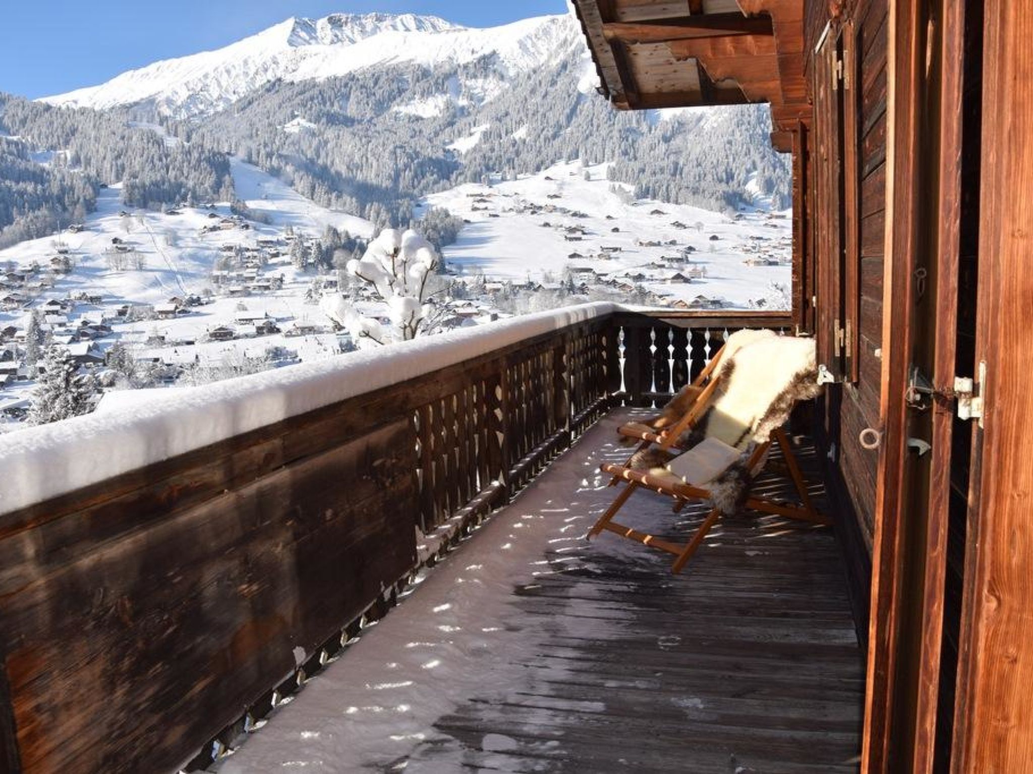 Un balcon en bois avec une chaise, donnant sur un paysage montagneux enneigé.