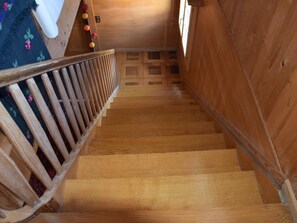 Eine Holztretreppe mit Handlauf, die zu einem Raum mit einem gemusterten Teppich führt.