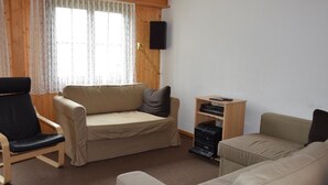 A living room with a sofa, a chair, a small table, and a television mounted on the wall. - Brandegg 4 Appartement/Fewo, Dusche oder Bad, WC 5-Bett-Wohnung by Interhome (Lenk)
