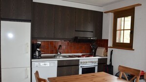 A compact kitchen with dark wood cabinets, a white refrigerator, a dishwasher, a stove, and a window with a view. - Brandegg 4 Appartement/Fewo, Dusche oder Bad, WC 5-Bett-Wohnung by Interhome (Lenk)