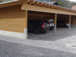 Un estacionamiento techado con dos autos estacionados bajo una estructura de madera.