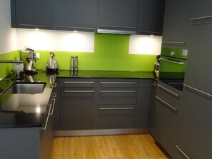 Una cocina con gabinetes grises, encimera negra y salpicadero verde.