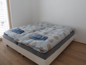 Ein Einzelbett mit einem gemusterten Bettüberwurf und zwei gefalteten Handtüchern.
