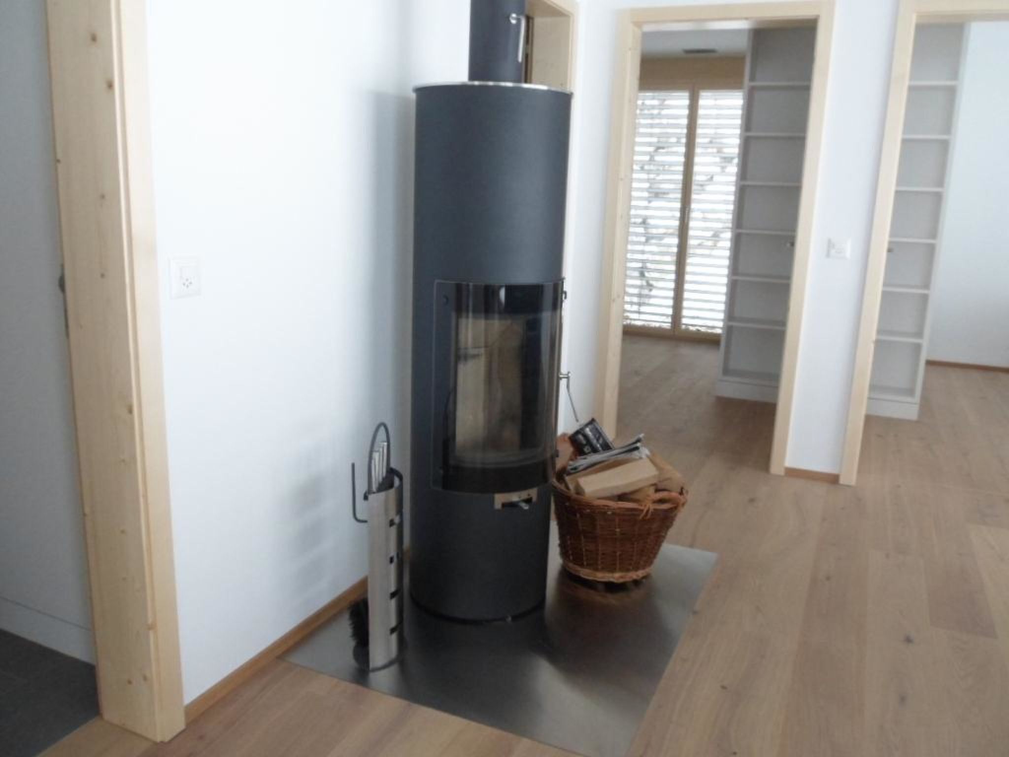 Ein Zimmer mit Kaminofen, Korb und Holzdielenboden.
