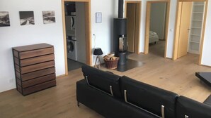 A modern living room with a black sofa, wooden flooring, a fireplace, and a kitchen area visible through an open door. - Chalet Coco Appartement/Fewo, Dusche, WC, 3 Schlafräume 6-Bett-Wohnung by Interhome (Lenk)