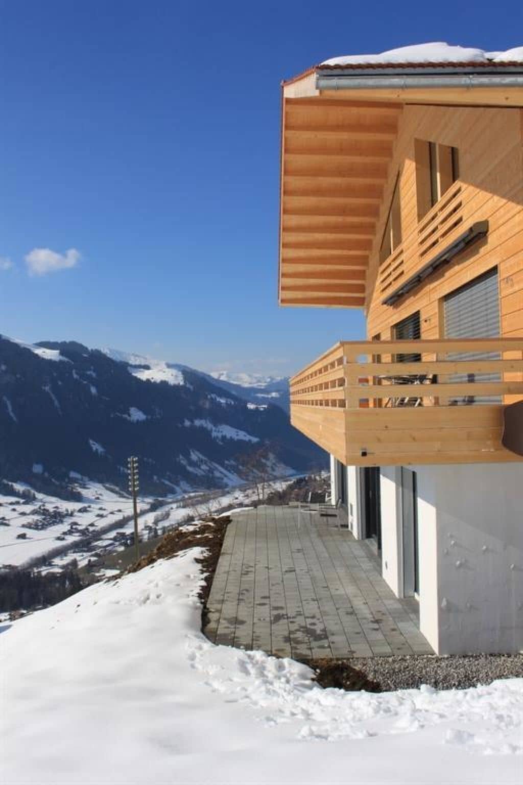 A modern building with a wooden facade, a balcony, and a view of snow-covered mountains.
