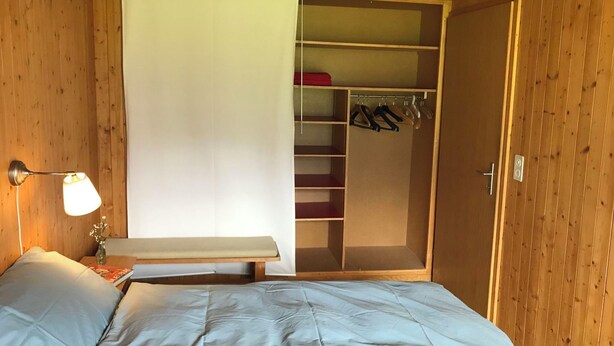 Ein Schlafzimmer mit Bett, Nachttisch, Lampe, Schrank und Kleiderhaken.