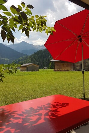Ein roter Regenschirm, eine Rasenfläche und eine Bergkulisse.
