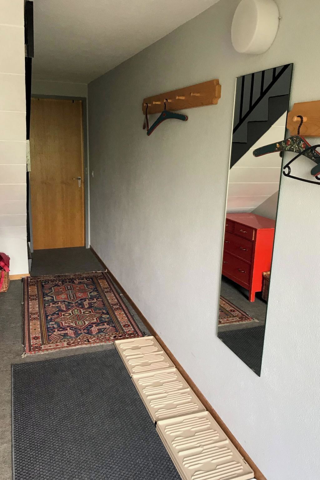 A hallway with a patterned rug, a wooden door, a mirror, and a red dresser.