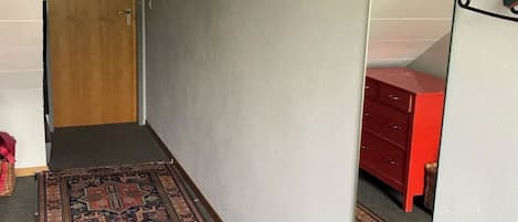 A hallway with a patterned rug, a wooden door, a mirror, and a red dresser.