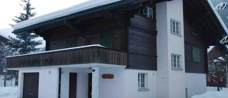 Un chalet de dos pisos con fachada de madera, un balcón y un techo cubierto de nieve.
