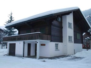 Eine zweistöckige Chalet mit Holzfassade, einem Balkon und einem mit Schnee bedeckten Dach.