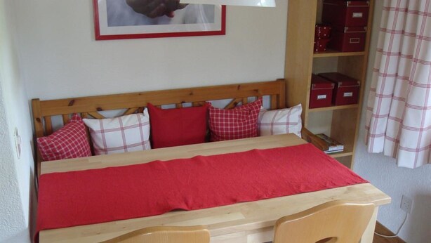 A room with a wooden bed, red bedding, and a wooden table with two chairs. - Elena # 1 Appartement/Fewo, Dusche oder Bad, WC, 1 Schlafraum 2-Bett-Wohnung by Interhome (Lenk)
