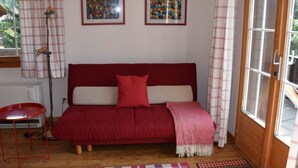 A cozy room with a red sofa, two framed artworks on the wall, a small red table, and a window with curtains. - Elena # 1 Appartement/Fewo, Dusche oder Bad, WC, 1 Schlafraum 2-Bett-Wohnung by Interhome (Lenk)
