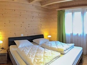 Un lit double avec une couette matelassée et des oreillers, une tête de lit en bois, une table de chevet avec une lampe et une fenêtre avec des rideaux.