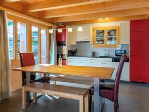 A wooden dining table with benches, a kitchen with red cabinets, and a stone wall. - Lemberg Ferienhaus, Dusche und Bad, WC, 3 Schlafräume 6-Bett-Ferienhaus by Interhome (Lenk)