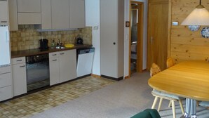 A compact kitchen with white cabinets, a sink, and a dining area with a table and chairs. - Reseda Appartement/Fewo, Dusche und Bad, WC, 2 Schlafräume 4-Bettwohnung by Interhome (Lenk)