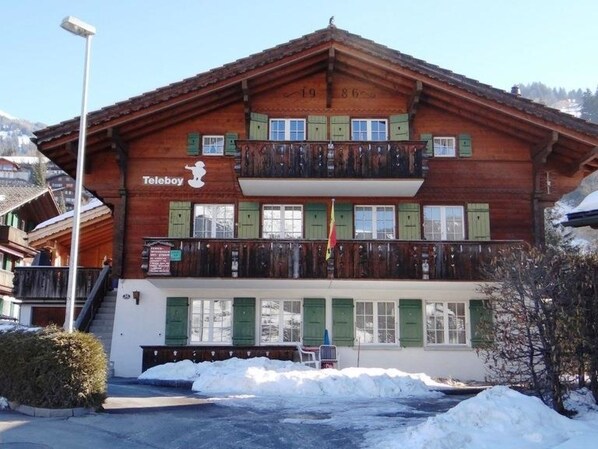 A two-story wooden building with a balcony, a sign for 'Teleboy,' and a flag. - Teleboy Appartement/Fewo, Dusche oder Bad, WC, 1 Schlafraum 4-Bett-Wohnung by Interhome (Lenk)