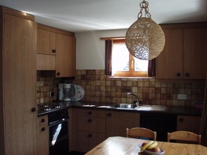 A kitchen with wooden cabinets, a stove, a sink, and a window with curtains. - Teleboy Appartement/Fewo, Dusche oder Bad, WC, 1 Schlafraum 4-Bett-Wohnung by Interhome (Lenk)