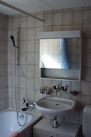 A bathroom with a bathtub, a sink, a mirror, and a shower. - Teleboy Appartement/Fewo, Dusche oder Bad, WC, 1 Schlafraum 4-Bett-Wohnung by Interhome (Lenk)