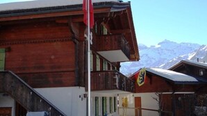 Een houten gebouw met balkon en vlag, omgeven door met sneeuw bedekte bergen.