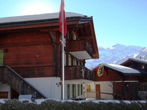 A wooden building with a balcony and a flag, surrounded by snow-covered mountains. - Teleboy Appartement/Fewo, Dusche oder Bad, WC, 1 Schlafraum 4-Bett-Wohnung by Interhome (Lenk)