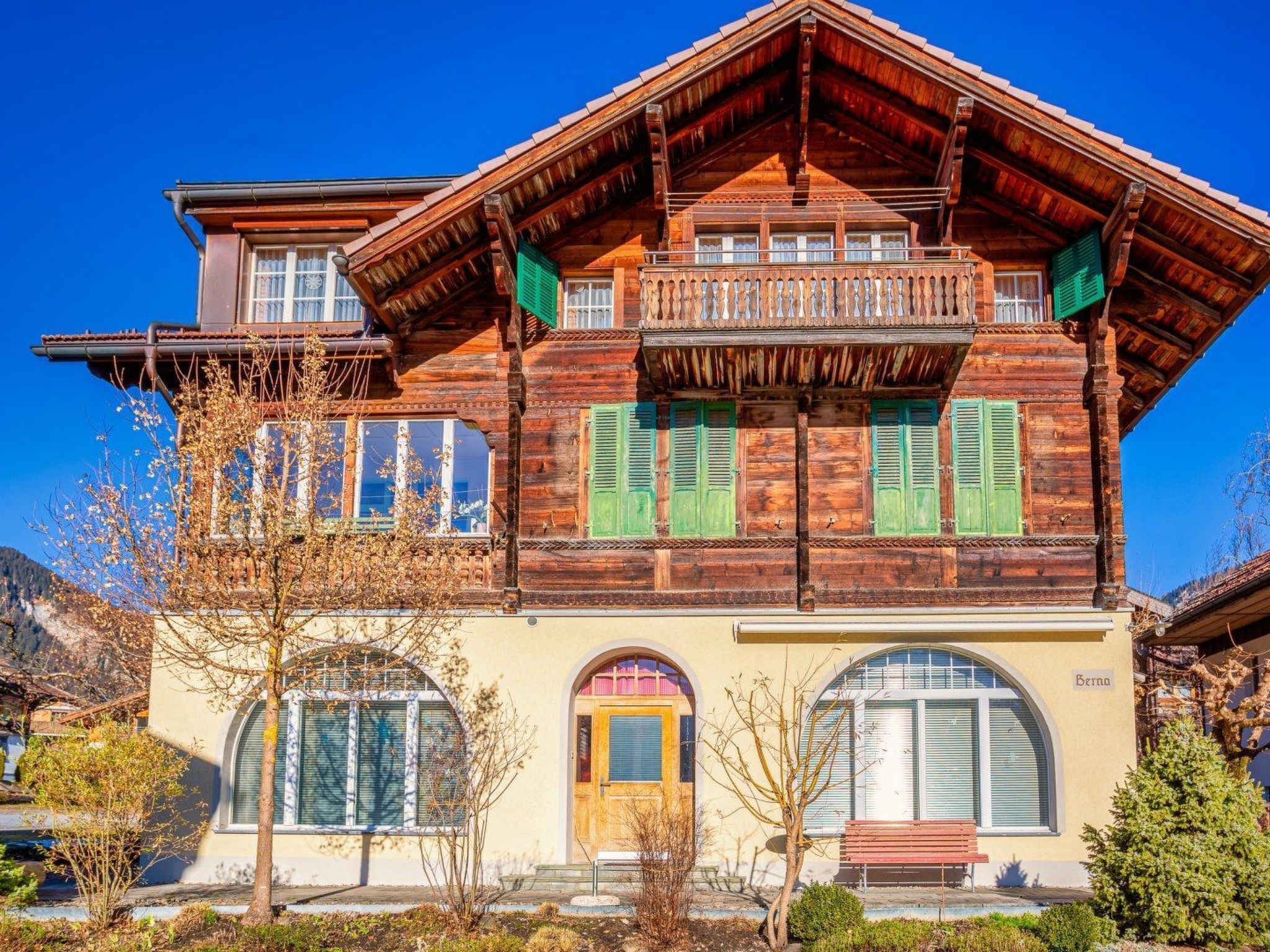 A traditional wooden house with a balcony, large windows, and a front door.
