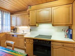 A kitchen with wooden cabinets, a stove, a sink, and a window with curtains. - Berna 2. Stock Appartement/Fewo, Bad, WC, 2 Schlafräume 4-Bettwohnung by Interhome (Lenk)