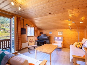 A cozy cabin interior with a wooden ceiling, a sofa, a table, and a piano. - Berna 2. Stock Appartement/Fewo, Bad, WC, 2 Schlafräume 4-Bettwohnung by Interhome (Lenk)