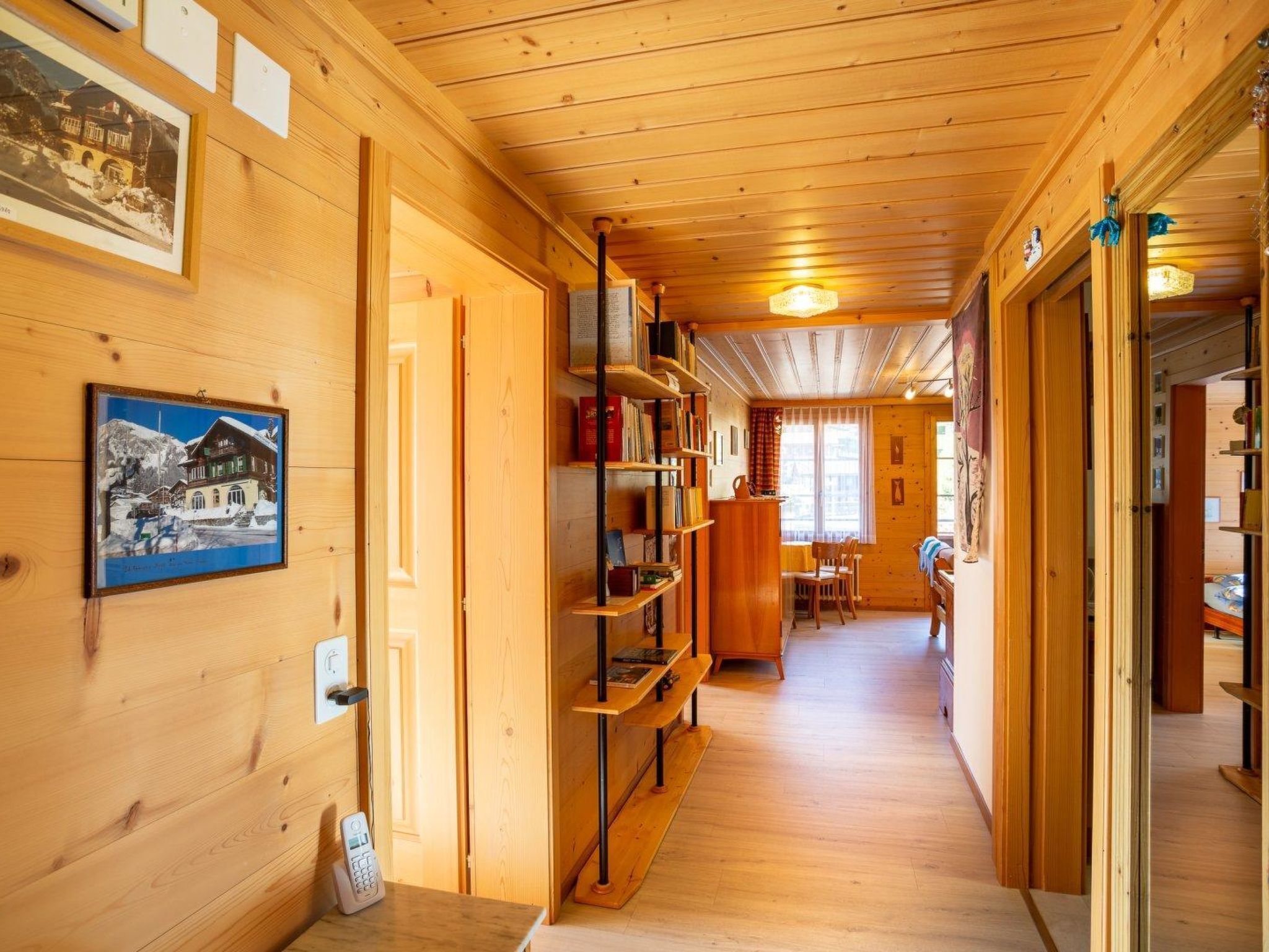 Un intérieur en bois comprenant un couloir, des étagères à livres, un coin repas et une cheminée.