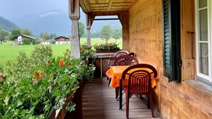 Une véranda en bois, avec une table et des chaises, donnant sur un paysage verdoyant et des maisons.
