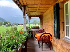 A wooden porch with a table and chairs, overlooking a green landscape and houses. - Bühlerhof Appartement/Fewo, Dusche oder Bad, WC, 3 Schlafräume 6-Bett-Wohnung by Interhome (Lenk)