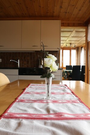 A dining table with a white and red patterned tablecloth, a clear glass vase with white flowers, and a wooden ceiling. - Bühlerhof Appartement/Fewo, Dusche oder Bad, WC, 3 Schlafräume 6-Bett-Wohnung by Interhome (Lenk)