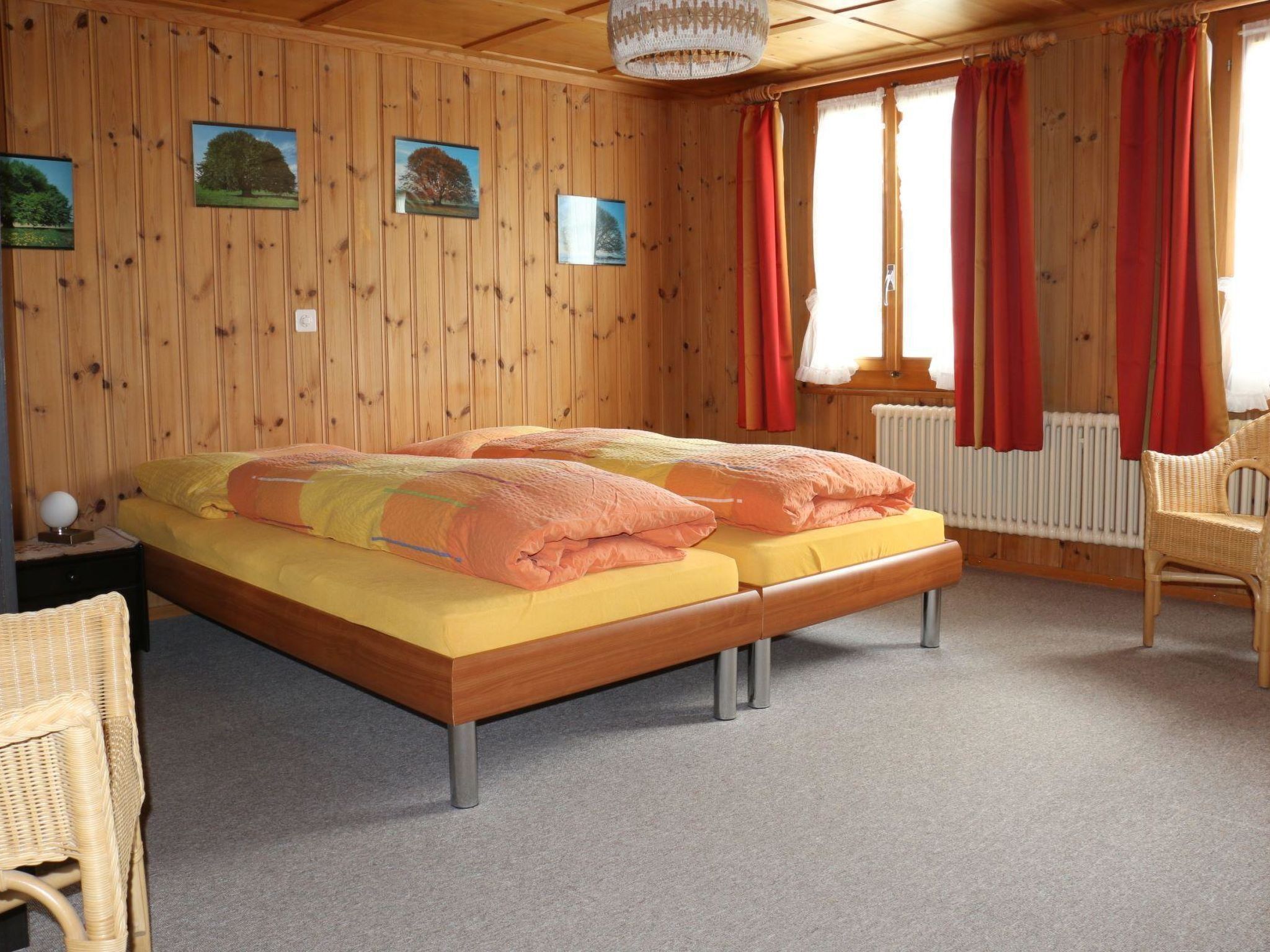 A wooden-paneled bedroom with a double bed, two side tables, a chair, and a window with red curtains.