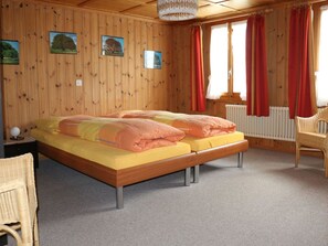 A wooden-paneled bedroom with a double bed, two side tables, a chair, and a window with red curtains. - Bühlerhof Appartement/Fewo, Dusche oder Bad, WC, 3 Schlafräume 6-Bett-Wohnung by Interhome (Lenk)