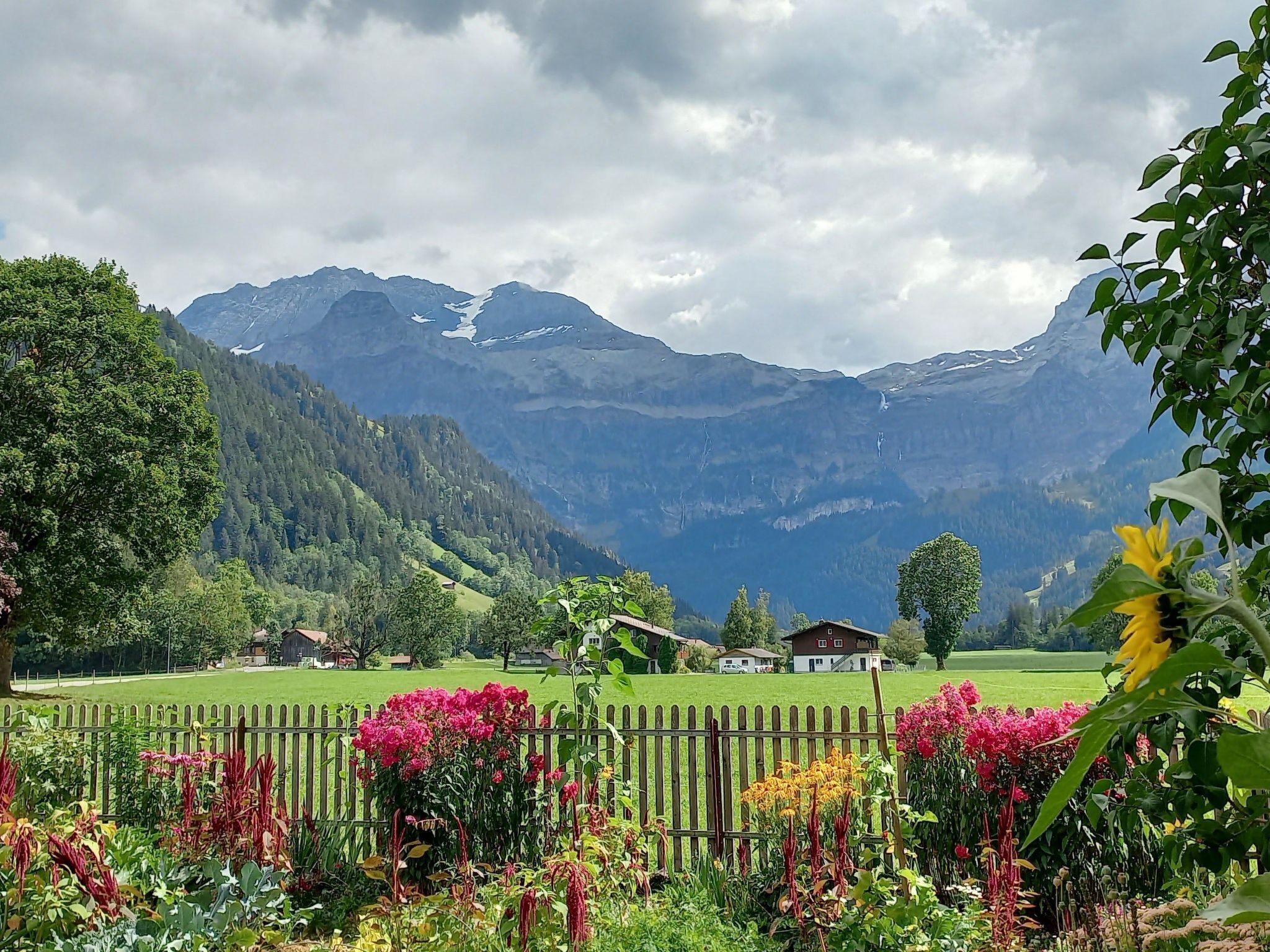 A mountainous landscape with a wooden fence and colorful flowers in the foreground.