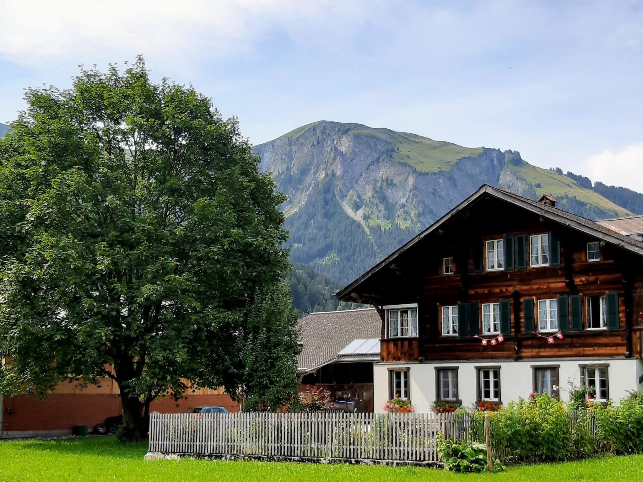 En traditionell chalet i trä med ett sluttande tak, omgiven av en välskött gräsmatta och ett trästaket.