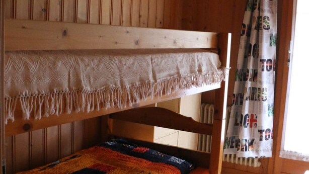 Un lit superposé avec une couverture à motifs et un tapis rouge sur le sol.