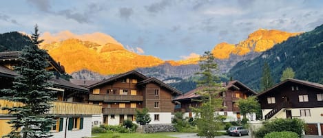 A chalet-style building with a wooden facade, surrounded by a well-maintained lawn and a mountain backdrop.