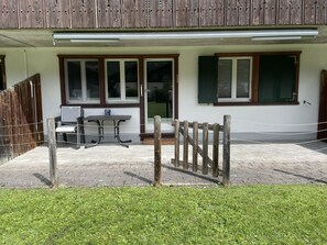 A building with a covered outdoor seating area, a wooden fence, and a paved entrance. - Bergecho EG Mitte Appartement/Fewo, Bad, WC, 1 Schlafraum 2 Bettwohnung by Interhome (Lenk)
