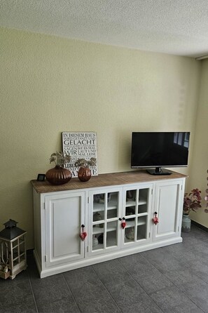 A room with a white cabinet, a television on top, and a sign on the wall.
