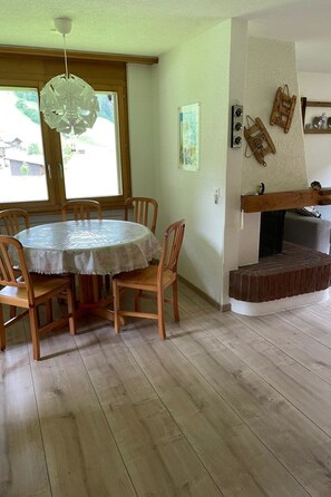 En matplats med ett runt bord och stolar, en hängande lampa och en öppen spis med en omramning av sten.