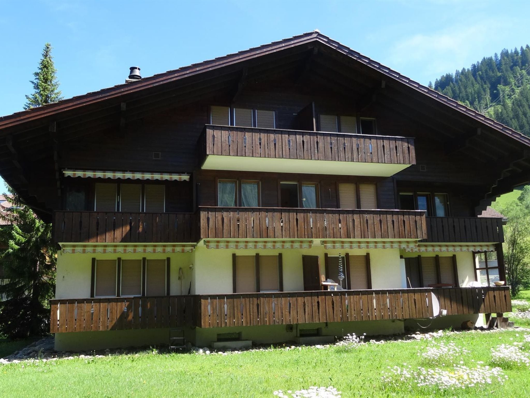 Un chalet en bois à plusieurs étages, doté de balcons, d’un porche avant couvert et surplombant un paysage montagneux.