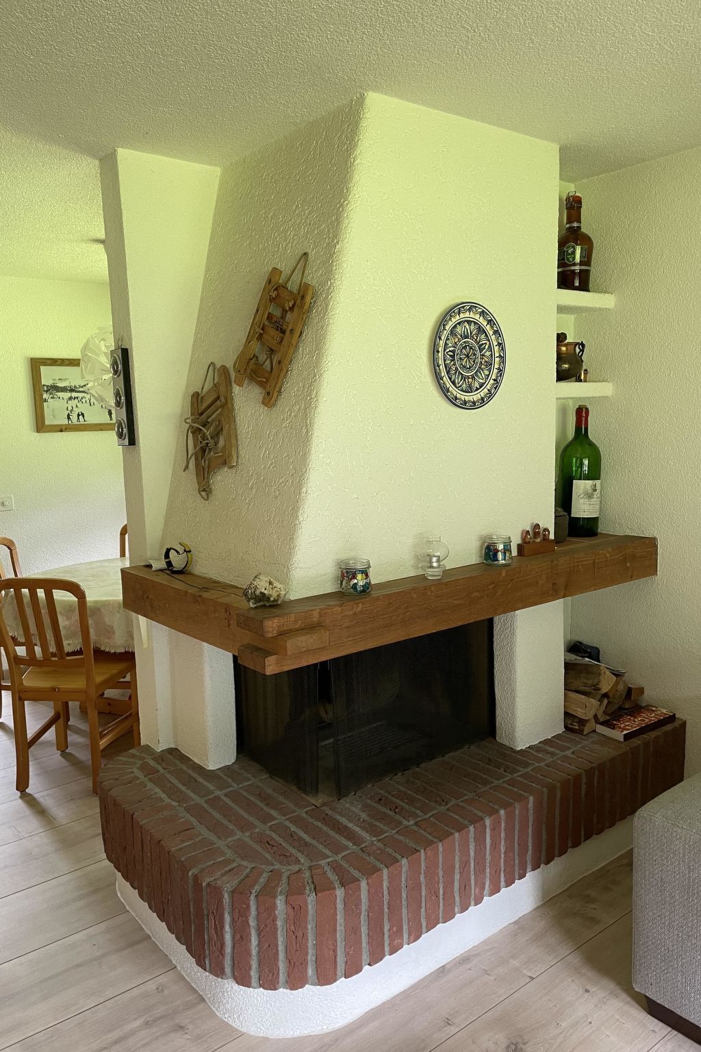 Un salon avec une cheminée, un banc en bois, une table avec des chaises et une étagère remplie de bouteilles.